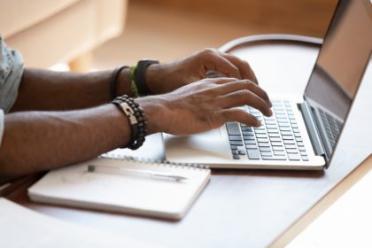 Close up cropped image young black man using laptop