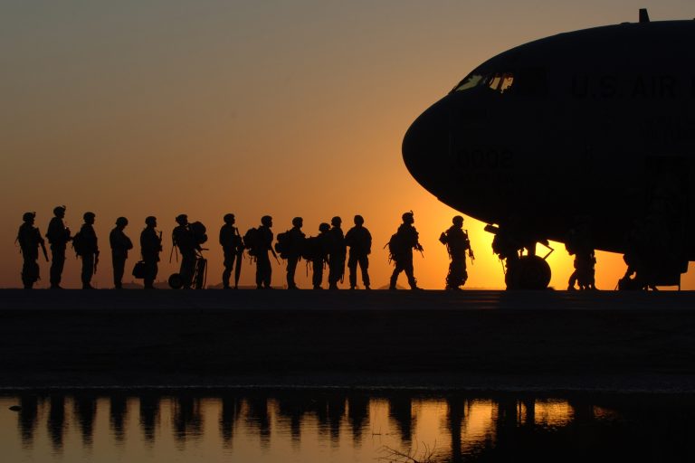 Silhouettes of service members walking toward a military aircraft at sunset